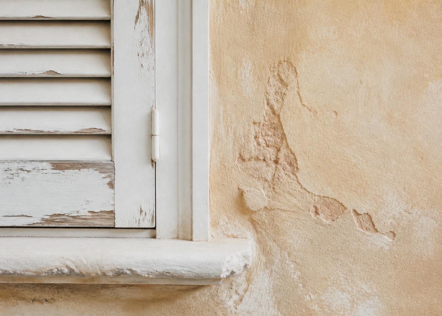 Weathered white shutters against a warm sand-colored coastal wall